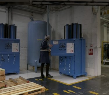 man in productieomgeving opent een blauwe balenpers met Mil-tek logo