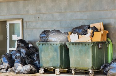 buitenstaande groene containers die overlopen met afval
